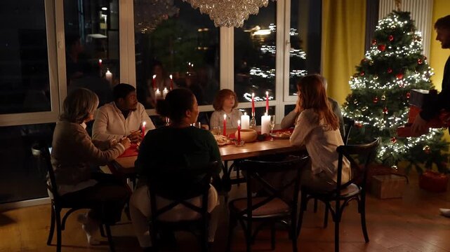Family sitting at the table talking while father takes presents from under the tree and gives them to his wife and grandfather