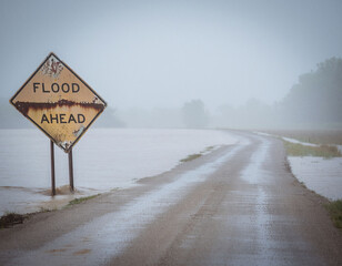 &ldquo;Flood ahead&rdquo; warning sign on rural road with fog and flooded roadway
