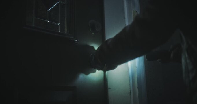 Low, handheld shot of woman with flashlight opening shadowy door and entering it