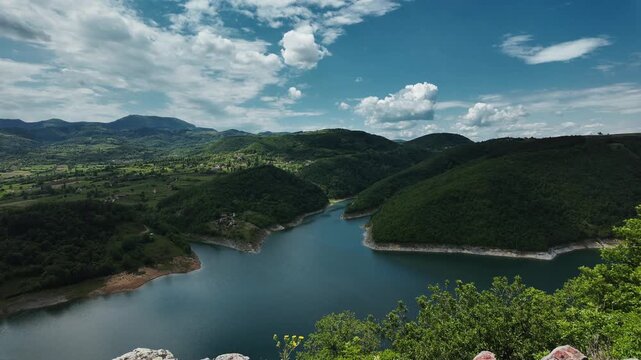 Timelapse view of Lake Rovni near Valjevo, Serbia. Scenic panorama of green hills and turquoise water under moving clouds in a dramatic summer sky