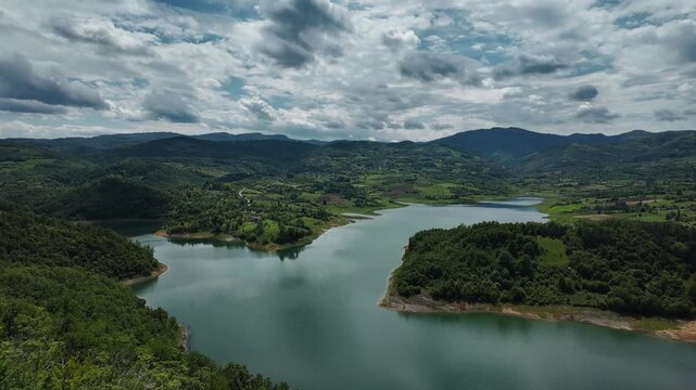 Timelapse view of Lake Rovni near Valjevo, Serbia. Scenic panorama of green hills and turquoise water under moving clouds in a dramatic summer sky
