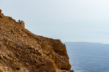 Fototapeta premium Ancient ruins of Masada fortress on a mountain top in the Judean Desert, Israel, overlooking the Dead Sea under a clear spring sky. Historical archaeological site and famous landmark at sunrise.