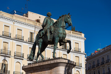 Equestrian statue of King Philip III at Plaza Mayor in Madrid, Spain, historic landmark surrounded by colorful facades and towers under a clear blue sky.
