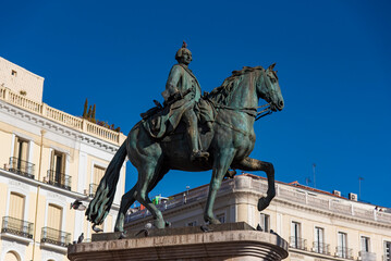 Obraz premium Equestrian statue of King Philip III at Plaza Mayor in Madrid, Spain, historic landmark surrounded by colorful facades and towers under a clear blue sky.