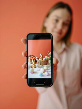 Person shows phone with easter decoration and sweet items in basket against orange wall