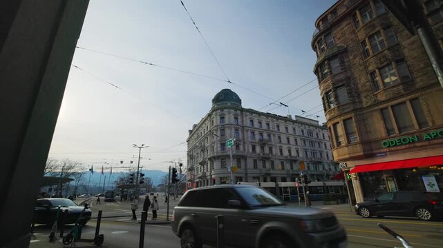 Static wide shot of Bellevue square in Zurich, Switzerland, featuring historic grand buildings like the Odeon Pharmacy, passing traffic, and a classic blue tram under a bright sky.