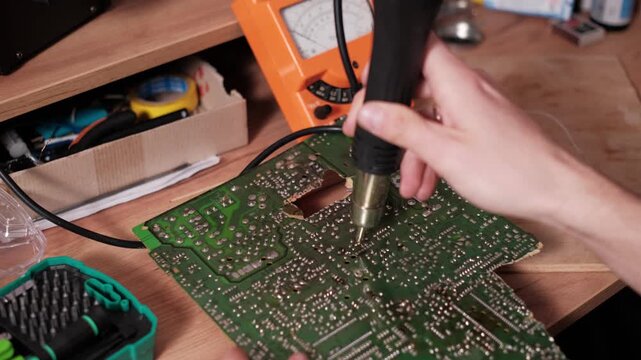 Close-up of a technician using a hot air rework station to heat components on a green circuit board. The process highlights advanced manufacturing and surface mount technology.