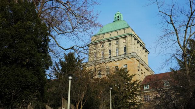 Panning shot of the iconic main building of the University of Zurich, featuring its historic stone tower with a distinctive green copper dome against a clear blue sky.