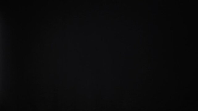 Two unrecognizable people bump their fists together in the center of the frame against a solid black background. The gesture symbolizes teamwork, agreement, and successful partnership.