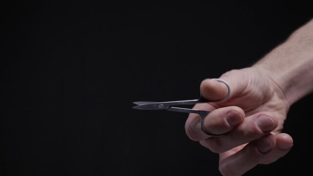 A male hand holds small silver scissors and mimics a cutting motion against a dark background. Ideally suited for concepts of grooming, precision, and personal hygiene care.