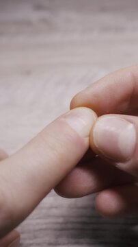 Person inspecting damaged cuticle and white spots on fingernail closely over a wooden table. This vertical video highlights nail health issues, dry skin, or personal grooming.