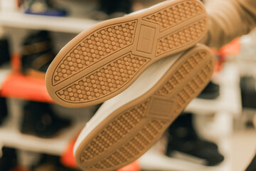 Close-up view of sneaker soles held by a person in a shoe store, showcasing detailed tread patterns and textures against a blurred background of footwear displays