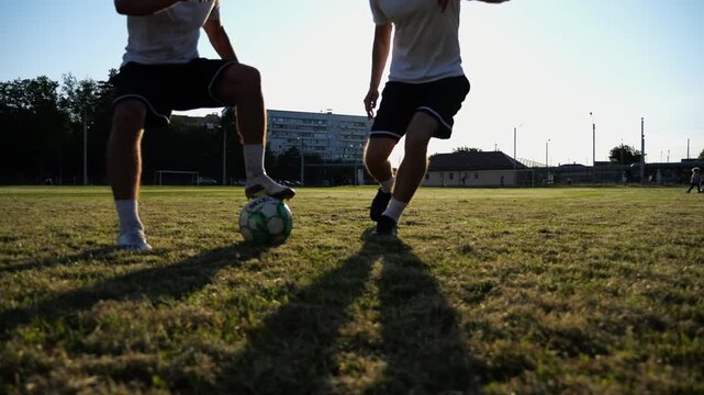 Two sportsmen playing in soccer in stadium at sunset. Professional footballers performing tricks with ball at green field. Young men training at meadow. Concept of a freestyle football. Slow motion