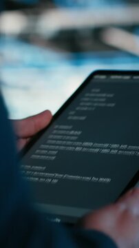Vertical video Close up of data center engineer using tablet to write code, compiling software patches to fix bugs. Server farm IT professional using device application to run programming script