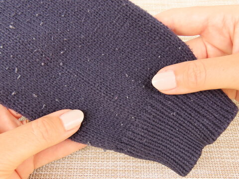 Closeup of woman hands holding dark blue sweater with pills. Sweater cuff with pills, also known as lint balls or fuzz.	