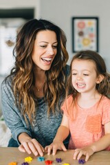 Obraz premium Mothers Day, Valentines Day, love holiday theme. A woman and a young girl playing with colorful jigsaw puzzle pieces on a table. The woman, wearing a gray and blue dress, and the girl.