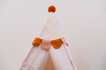 Play tipi tent with orange pompom on top, for kids playroom interior design, fun activity space for creative child play at home.