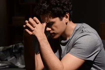 Fototapeta premium Sad young man sitting on sofa in dark room. International Stress Awareness Week