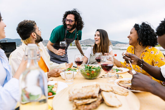 Group of young friends having dinner at home terrace. Millennial people enjoying time together sitting on table at summer party celebration. Friendship concept