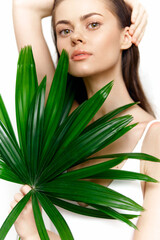 Naklejka premium Elegant woman holding tropical palm leaves, showcasing natural beauty and freshness in a minimalistic white background, ideal for seasonal projects.
