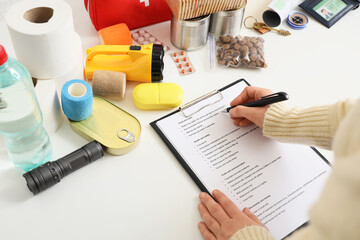 Young woman with check list of necessities for emergency backpack at home, closeup