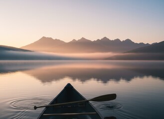Canoe Paddle on Calm Lake at Sunrise with Misty Mountain Range Reflection and Golden Hour Light