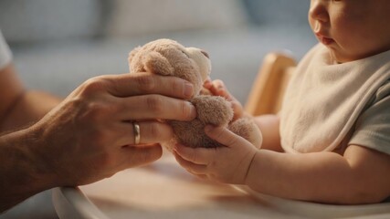 Father's hands giving a soft teddy bear to baby in a high chair, fostering family love and childhood connection