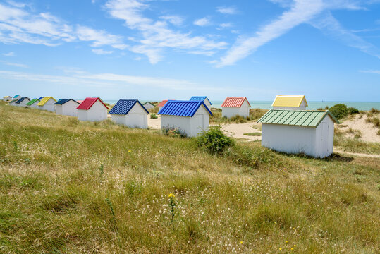 Rows of beach huts with colourful corrugated iron roofs along a sandy beach under blue sky on a clear summer day