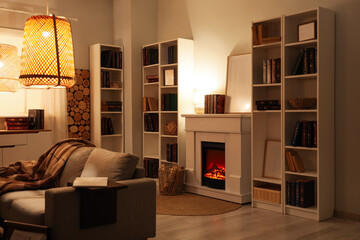 Interior of stylish living room with grey sofa, fireplace and bookshelves at evening © Pixel-Shot
