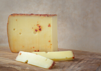 A cut piece of cheese with pepper on a wooden board with a beige background, selective focus, with copy space
