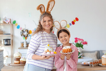 Happy mother with her daughter holding Easter cakes and eggs in kitchen
