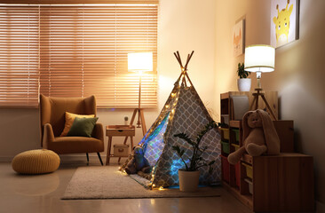 Interior of children's room with armchair, play tent and glowing lamps at night © Pixel-Shot