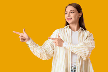 Fototapeta premium Beautiful happy young woman pointing at something on yellow background