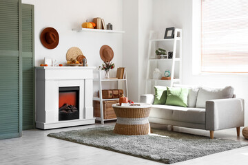 Naklejka premium Stylish living room with white fireplace, soft sofa, coffee table and pumpkins. Autumn concept