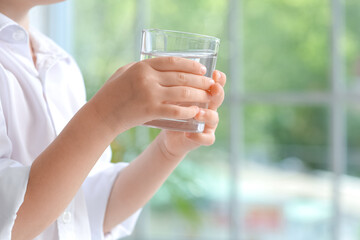 Cute little girl with glass of water near window at home, closeup