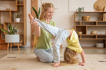 Obraz premium Beautiful young sporty woman with her little daughter practising yoga in living room