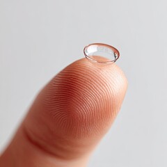 A clear, soft contact lens rests on a human fingertip, ready for insertion