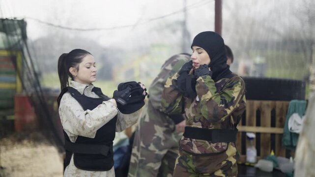 Group of friends prepares for a dynamic paintball or laser tag game, meticulously putting on their camouflage outfits and protective equipment.