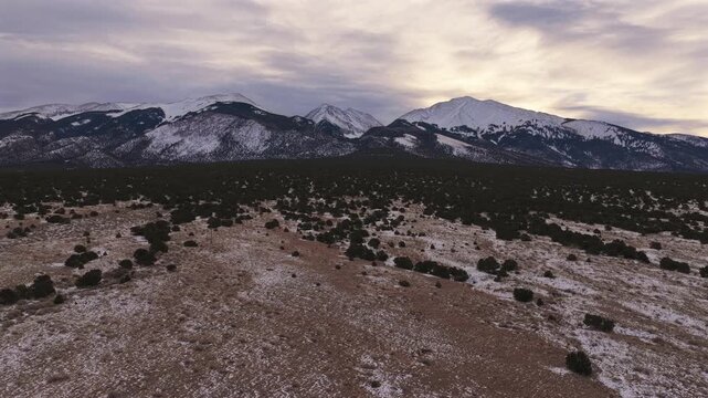 A lateral drone strafe captures the vast scale of snow-dusted Colorado peaks. This 4K cinematic shot features jagged alpine ridges rising above a rugged, high-altitude desert landscape.