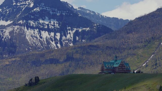 Prince of Wales Hotel standing on a green hill with snow capped mountains in Waterton national park