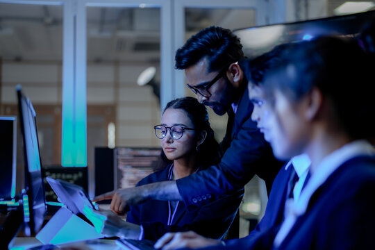 Senior software architect mentoring diverse development team on backend code. Agile scrum master leading sprint review in modern blue light tech office.