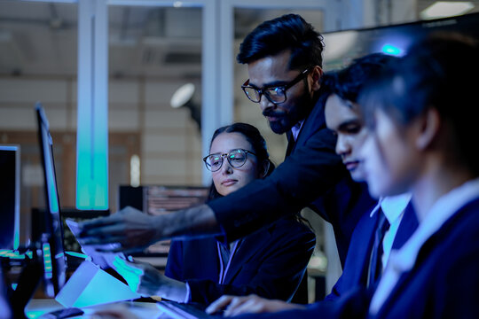 Senior software architect mentoring diverse development team on backend code. Agile scrum master leading sprint review in modern blue light tech office.