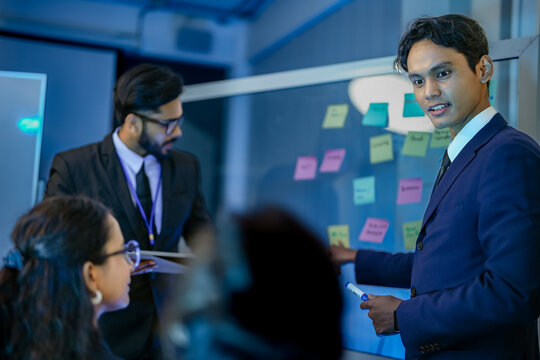 Agile scrum master facilitating sprint planning session utilizing kanban visualization on glass board. Technical product owner prioritizing backlog iteration tasks.