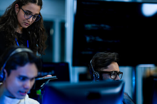 Corporate training mentor coaching technical workforce on operational standards. Diverse helpdesk team executing customer retention strategies in blue light environment.