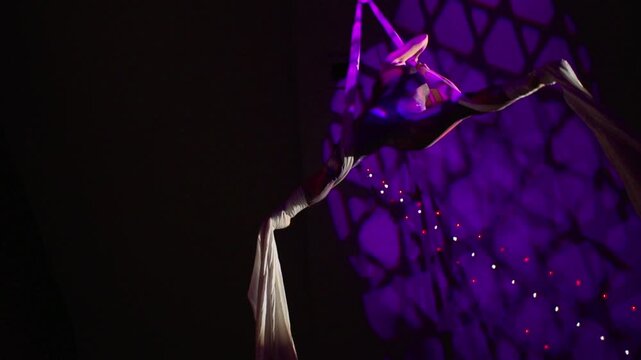 A beautiful performance by an agile aerial silk performer under the purple light