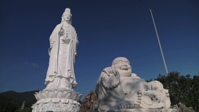 Da Nang, Vietnam White Guanyin And Laughing Buddha Statues Stand On Lotus Pedestals Against Deep Blue Sky Over Coastal Hills In Da Nang Vietnam, Carved Marble Texture, Serene Spiritual