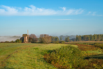 An ancient wooden windmill on the banks of the Sorot River on a foggy summer morning, Mikhailovskoye, Pushkinskiye Gory, Pskov region, Russia