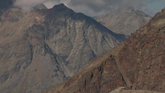 Two mountain bikers standing on the edge of a mountain ridge in Saas-Grund, Valais, enjoying sweeping views over the Swiss Alps. Calm high-altitude moment, scenic panorama, and cinematic adventure moo