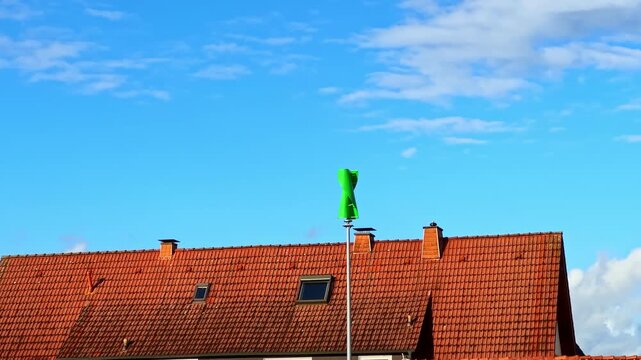 Bright green windsock waves cheerfully at the top of a post, contrasting against the blue sky and charming rooftops, creating a lively scene on a sunny day.