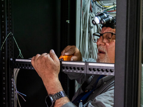 Senior technician installing network cables in data rack cabinet